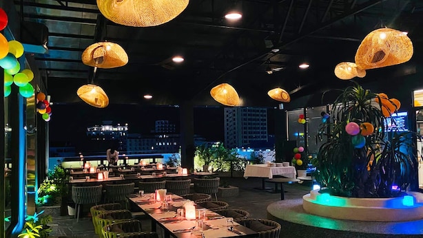 Un espacio de comedor al aire libre con sillas y mesas de mimbre, iluminado por lámparas colgantes de mimbre.