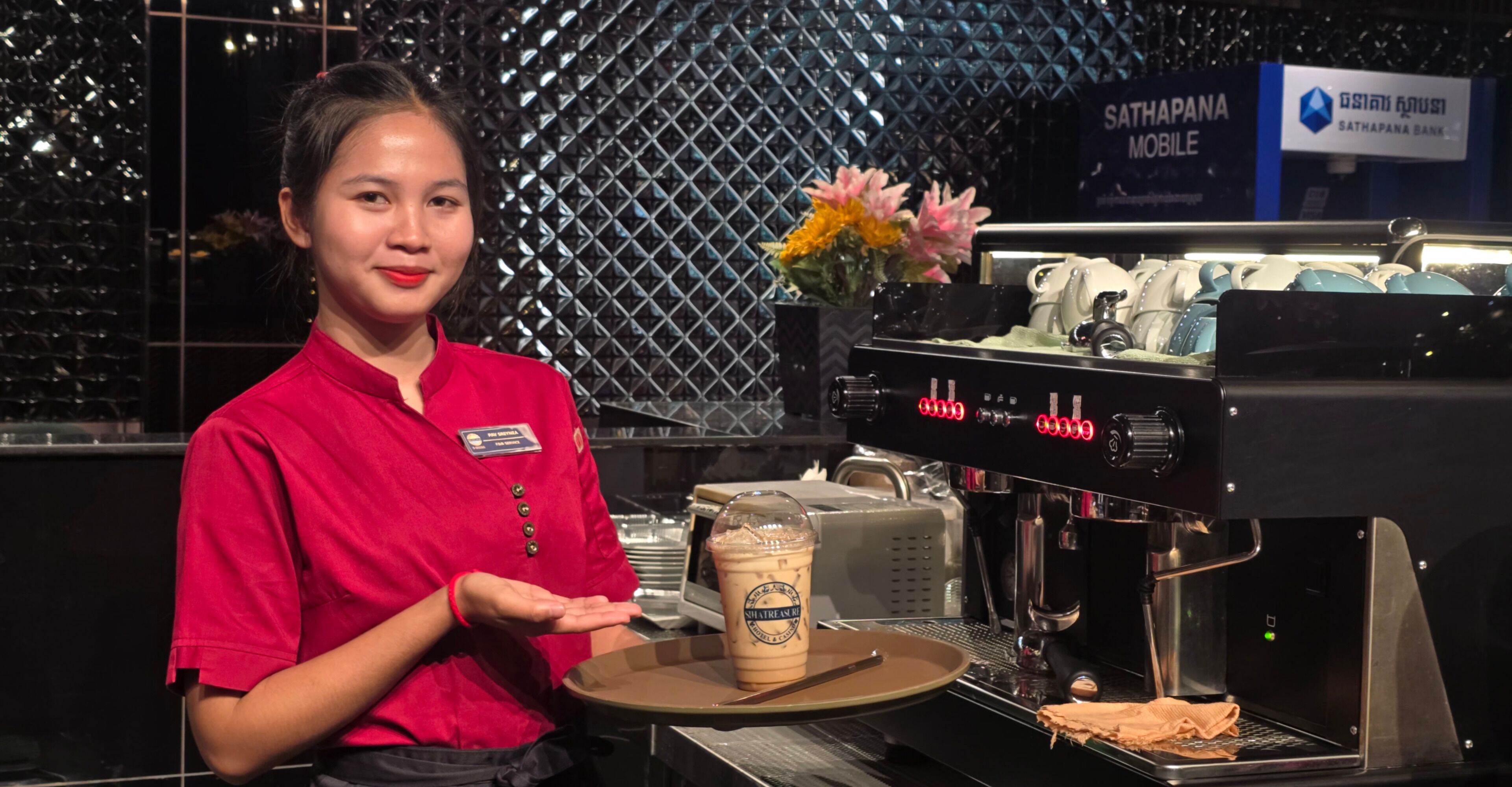 A barista in a red uniform presenting a beverage to a customer.