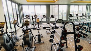 Un gimnasio con máquinas de cardio, equipo de levantamiento de pesas y amplios ventanales con vistas a la ciudad.