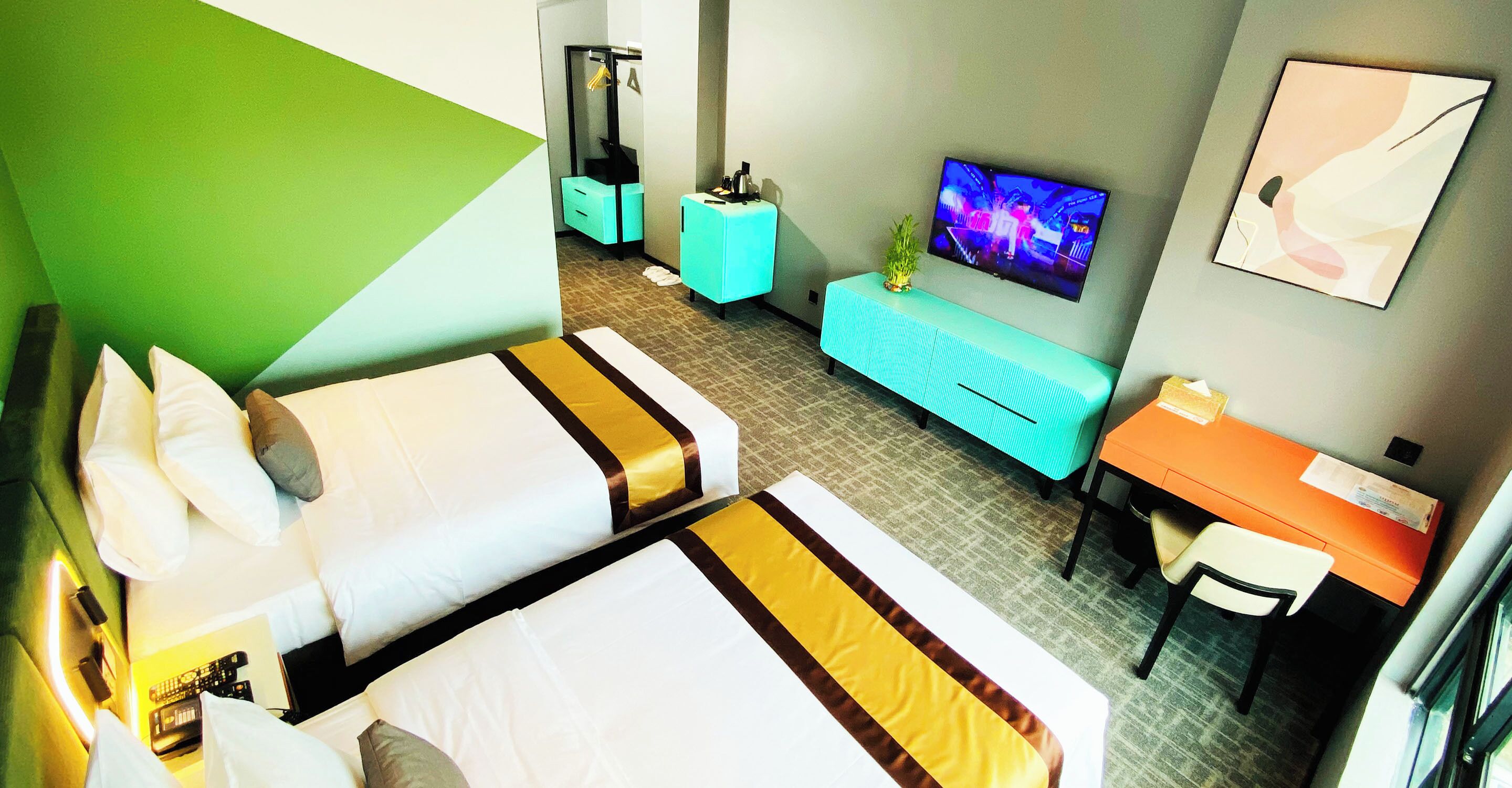 Ein Hotelzimmer mit zwei Betten, einem Schreibtisch, einem Fernseher und einer kleinen Pflanze.