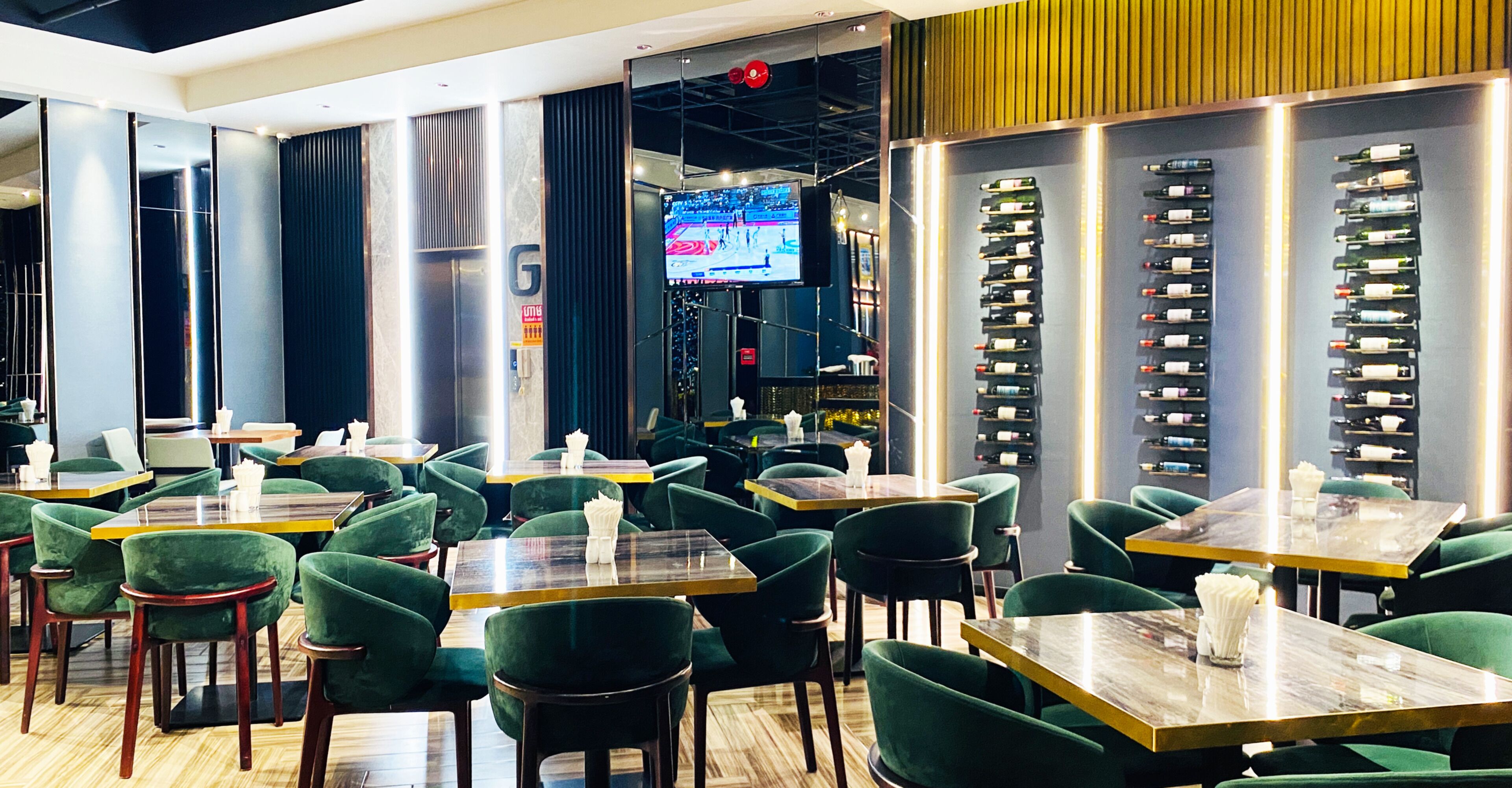 A restaurant with green upholstered chairs, wooden tables, and a wall-mounted wine rack.