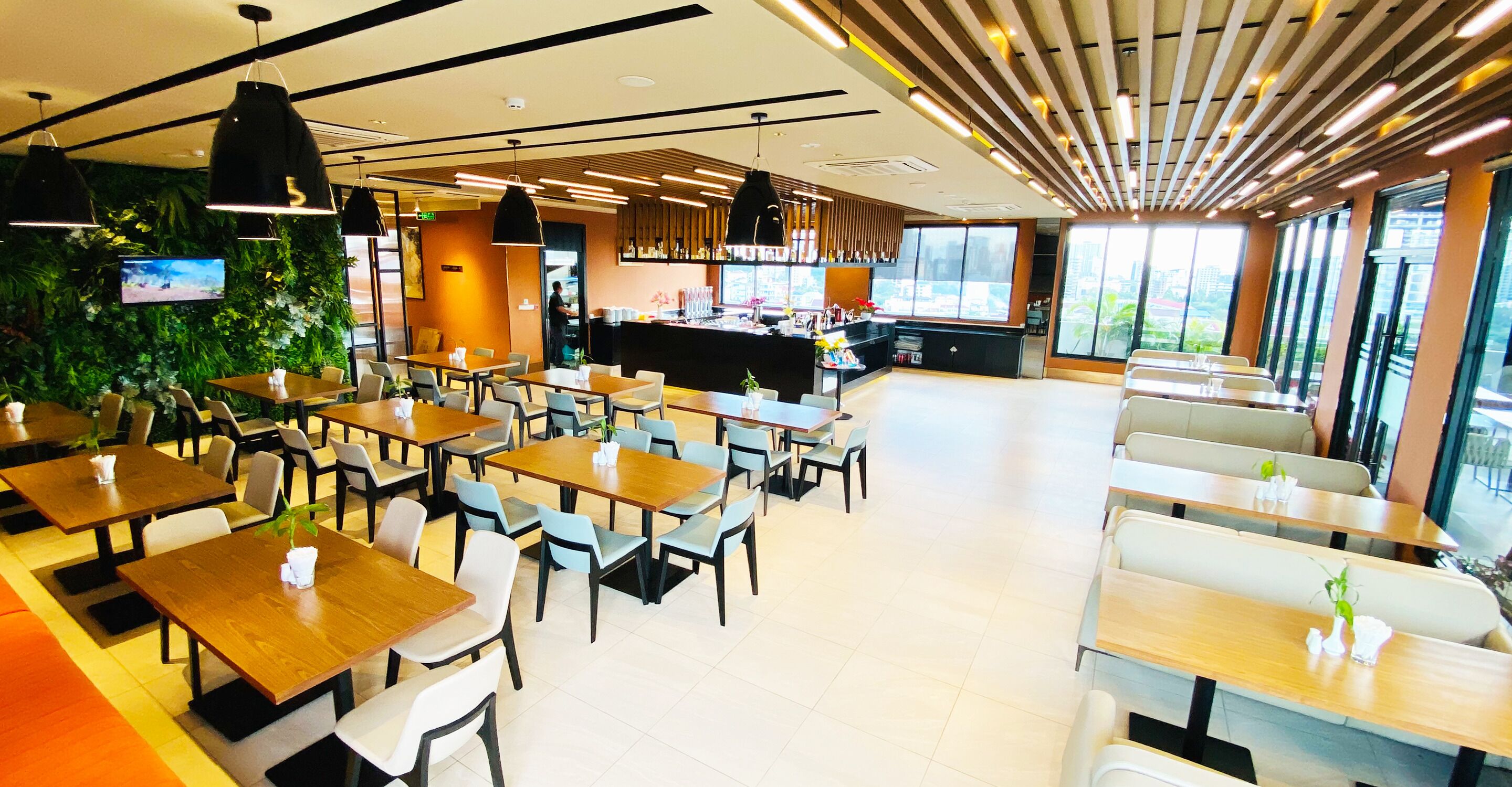 A modern restaurant with multiple dining tables and chairs, a bar area, and large windows providing a view of the city.