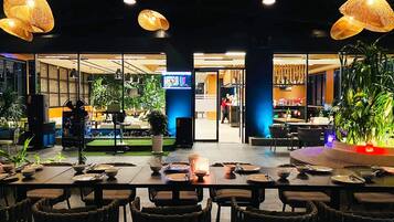 A restaurant with tables set for dining, a digital menu display, and indoor plants.