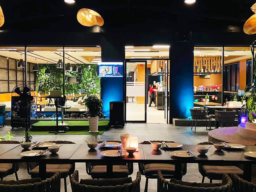A restaurant with tables set for dining, a digital menu display, and indoor plants.