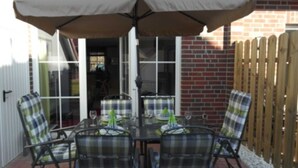 An outdoor patio with a table and four chairs, an umbrella, and a brick wall. - ROB 10 for 6 people, approx. 78 sqm - holiday village Robbenplatte Burhave (2) (Butjadingen)