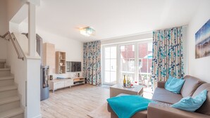 A modern living room with a staircase, a flat-screen TV, a sofa, and a dining area. - ROB 11 for 5 persons, approx. 78 sqm, sauna - Feriendorf Robbenplatte Burhave (2) (Butjadingen)