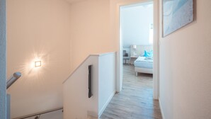 A staircase leading to a bedroom with a bed, a nightstand, and a wall-mounted light fixture. - ROB 11 for 5 persons, approx. 78 sqm, sauna - Feriendorf Robbenplatte Burhave (2) (Butjadingen)