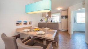 A modern dining area with a table set for two, a hanging light fixture, and a view of the kitchen in the background. - ROB 11 for 5 persons, approx. 78 sqm, sauna - Feriendorf Robbenplatte Burhave (2) (Butjadingen)