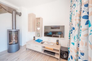 A modern living room with a wood-burning stove, a TV mounted on the wall, a wooden cabinet, and a curtain with a leaf pattern.