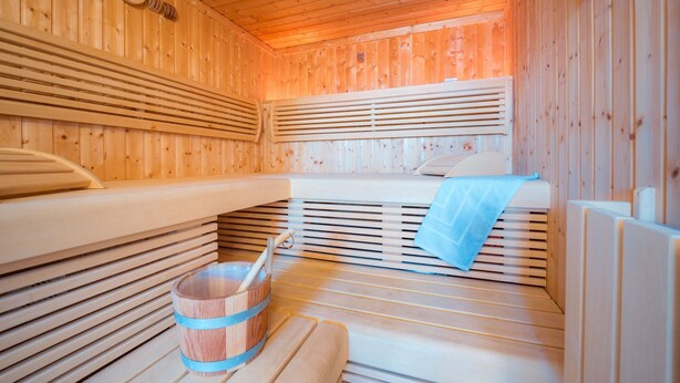 A sauna with wooden walls and benches, a clock, and a bucket with a brush. - ROB 11 for 5 persons, approx. 78 sqm, sauna - Feriendorf Robbenplatte Burhave (2) (Butjadingen)