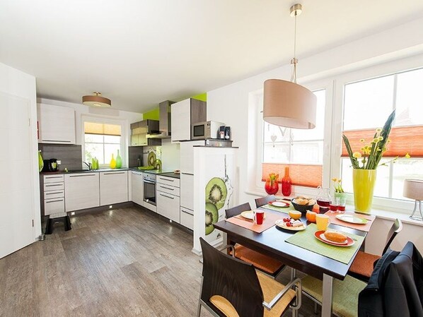 A modern kitchen with white cabinets, a dining area with a table set for two, and a large window providing natural light.