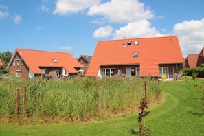 A row of red-roofed houses with a grassy lawn and a clear blue sky.