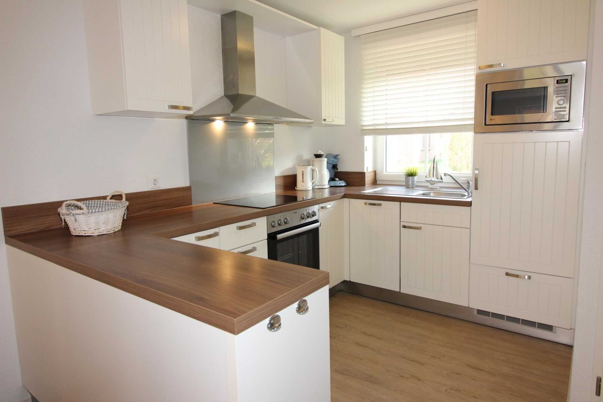 Una cocina compacta con armarios blancos, una campana extractora de acero inoxidable, un microondas y un horno empotrado.