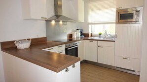 A compact kitchen with white cabinetry, a stainless steel range hood, a microwave, and a built-in oven. - ROB 14 for 6 persons, approx. 86 sqm, pets, sauna - Feriendorf Robbenplatte (Butjadingen)