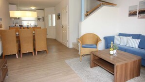 A modern living room with a blue sofa, a wooden coffee table, and wicker chairs. A staircase leads to an upper level. - ROB 14 for 6 persons, approx. 86 sqm, pets, sauna - Feriendorf Robbenplatte (Butjadingen)