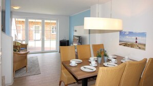 A dining area with a table set for four, wicker chairs, a large hanging lamp, and a painting of a lighthouse on the wall. - ROB 14 for 6 persons, approx. 86 sqm, pets, sauna - Feriendorf Robbenplatte (Butjadingen)