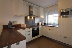 A modern kitchen with white cabinetry, a stainless steel range hood, an oven, a microwave, and a coffee maker.