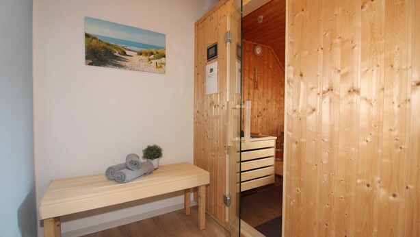 A wooden sauna room with a bench, a small plant, and a picture on the wall. - ROB 14 for 6 persons, approx. 86 sqm, pets, sauna - Feriendorf Robbenplatte (Butjadingen)