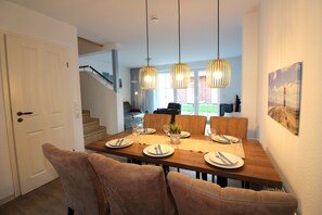 A dining area with a wooden table set for four, two pendant lights, and a view of a staircase leading to another room. - ROB 14 for 6 people, approximately 86 m², pets allowed, sauna - Robbenplatte Vacation Village   (Butjadingen)