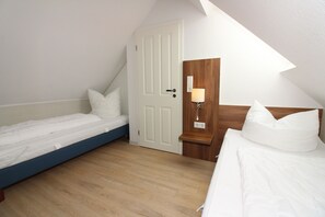 A small, single-room bedroom with a sloped ceiling, a wooden door, a bedside table with a lamp, and two beds. - ROB 14 for 6 people, approximately 86 m², pets allowed, sauna - Robbenplatte Vacation Village   (Butjadingen)