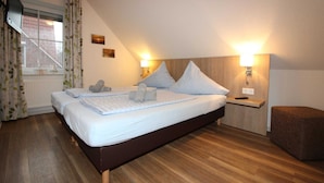 A bedroom with two beds, a window with curtains, a bedside table with a lamp, and a small ottoman. - ROB 15 for 8 persons, approx. 86 sqm - Feriendorf Robbenplatte Burhave (2) (Butjadingen)