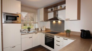 A modern kitchen with white cabinetry, a built-in microwave, a stove, and a coffee maker. - ROB 15 for 8 persons, approx. 86 sqm - Feriendorf Robbenplatte Burhave (2) (Butjadingen)