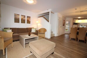 A living room with a sofa, armchair, ottoman, coffee table, and a staircase leading to another room. - ROB 15 for 8 persons, approx. 86 sqm - Feriendorf Robbenplatte Burhave (2) (Butjadingen)