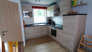 Een kleine keuken met lichte houten kastjes, een magnetron en een kookplaat.
