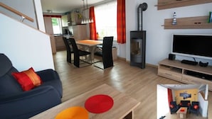 Een moderne woonkamer met een bank, een televisie en een open haard. Er is een eethoek met een tafel en stoelen.