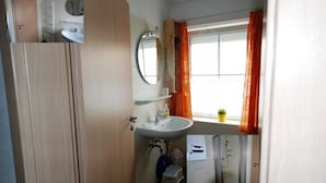 Een kleine badkamer met een wastafel, spiegel en raam met gordijnen.