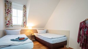 Een kleine, gezellige kamer met twee eenpersoonsbedden, een nachtkastje, een lamp en een raam met gordijnen.
