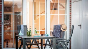 Een terras met een tafel en stoelen, een hoed op een stoel, en uitzicht door een glazen deur.