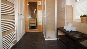 A shower area with a glass door, a bench with towels, and a wooden door with a towel rack. - ROB 20 for 8 persons, approx. 86 sqm, pets, sauna - Feriendorf Robbenplatte (Butjadingen)