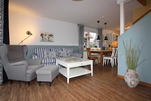 Un salon comprenant un fauteuil gris, un canapé à rayures, une table basse blanche et un coin repas avec une table et des chaises en bois.