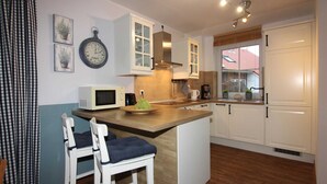 A compact kitchen with white cabinets, a microwave, a sink, and a window with a view of a red-roofed building. - ROB 20 for 8 persons, approx. 86 sqm, pets, sauna - Feriendorf Robbenplatte (Butjadingen)