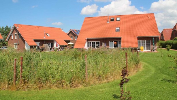 A row of red-roofed houses with a grassy lawn and a clear blue sky. - ROB 18 for 6 persons, approx. 86 sqm - Feriendorf Robbenplatte Burhave (3) (Butjadingen)
