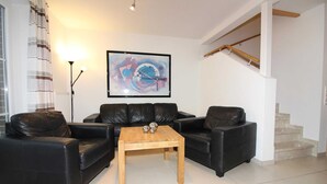 A living room with a black leather sofa set, a wooden coffee table, and a large abstract painting on the wall. - ROB 18 for 6 persons, approx. 86 sqm - Feriendorf Robbenplatte Burhave (3) (Butjadingen)