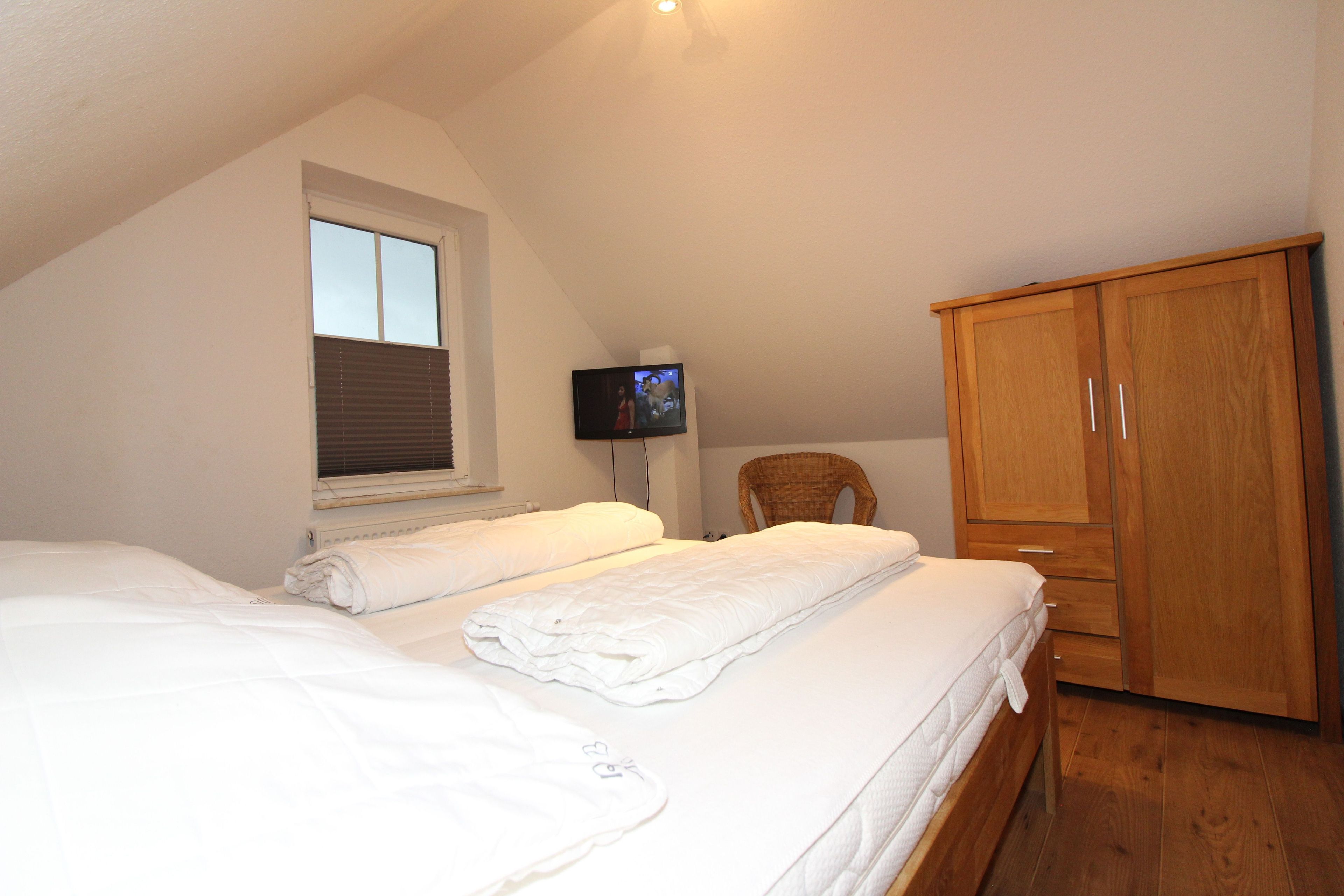 Quarto com duas camas, televisão, guarda-roupa de madeira e janela com persianas.