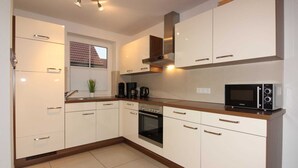 A modern kitchen with white cabinets, a built-in oven, a microwave, and a coffee maker. - ROB 18 for 6 persons, approx. 86 sqm - Feriendorf Robbenplatte Burhave (3) (Butjadingen)