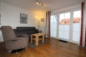 A living room with a sofa, armchair, and a small table with a bottle and glass.