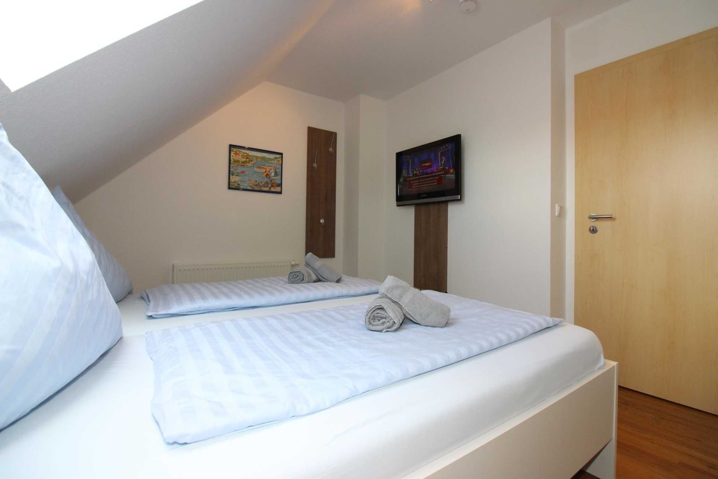 Una camera da letto con due letti, una televisione a parete e una porta.