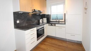 A compact kitchen with white cabinets, a black countertop, and a built-in oven. - ROB 19 for 6 persons, approx. 86 sqm, sauna - Feriendorf Robbenplatte Burhave (3) (Butjadingen)
