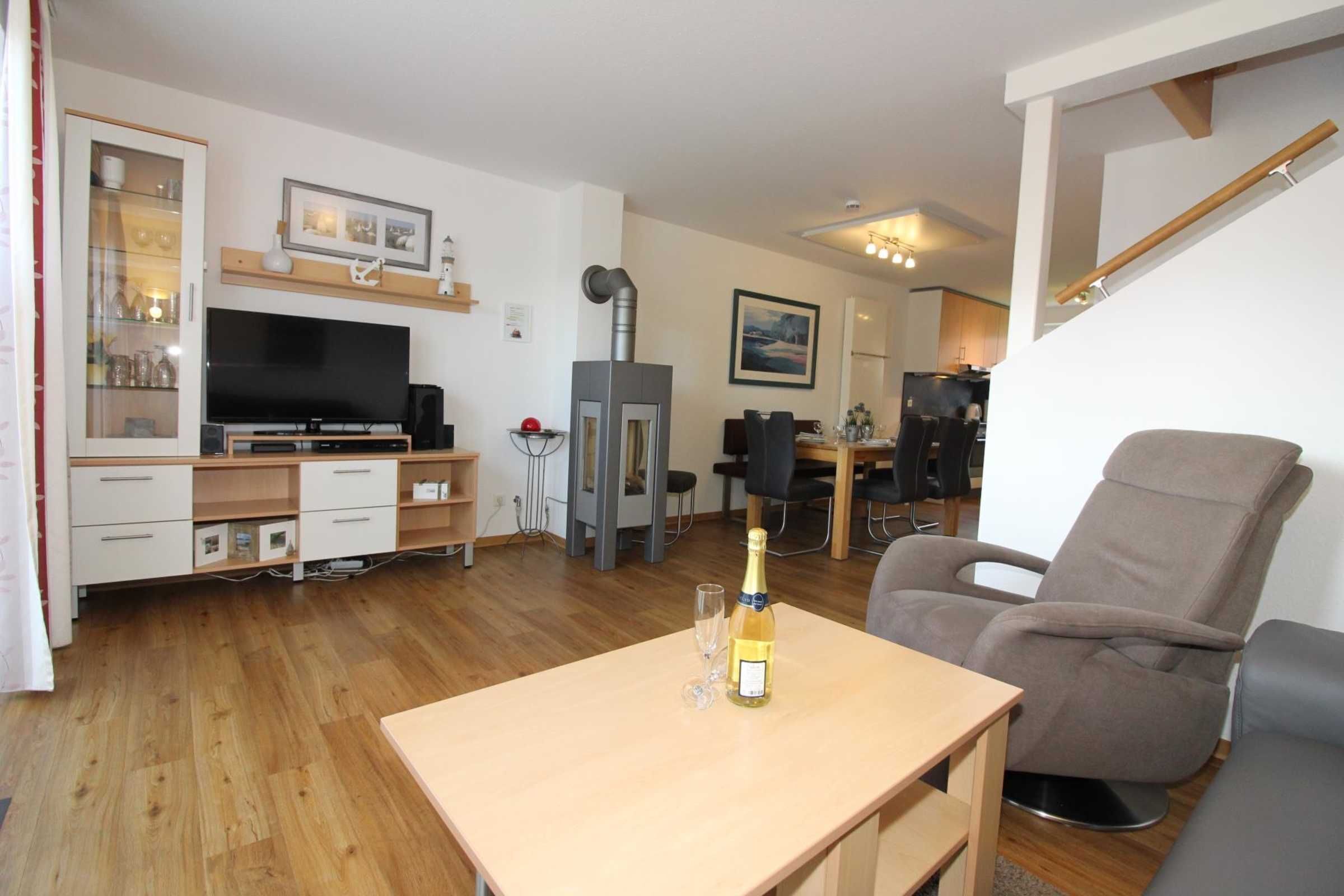 A modern living room with a flat-screen TV, a wooden cabinet, a fireplace, a dining area with a table and chairs, and a comfortable armchair.