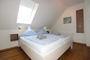 A bedroom with a sloped ceiling, two beds, a small bedside table, a radiator, and a wooden door.