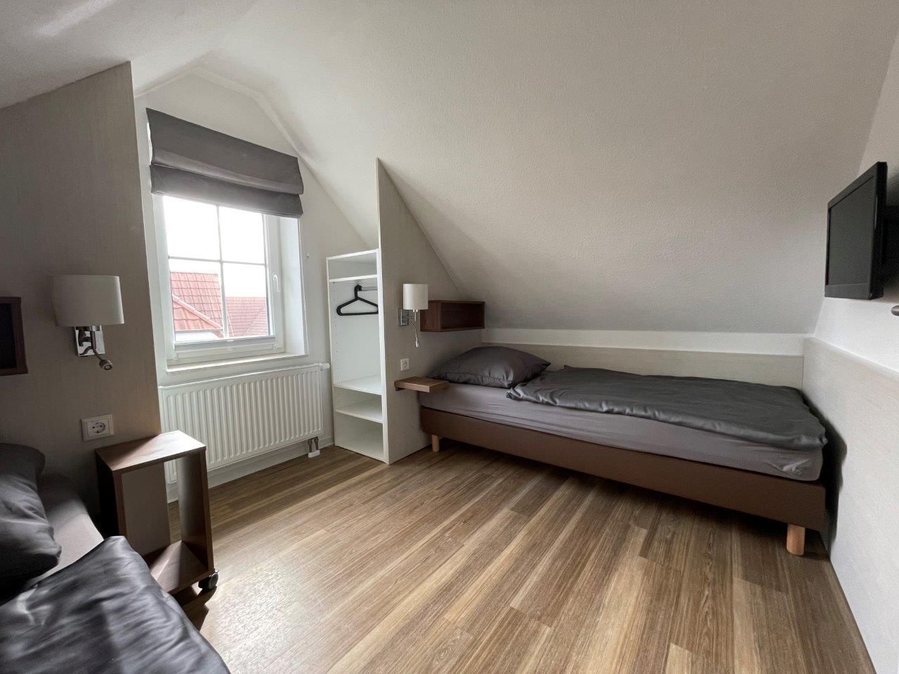 A small, modern bedroom with a loft bed, a bedside table, a hanging light, and a radiator.