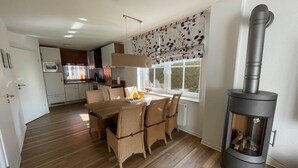 A modern kitchen with white cabinets, a microwave, and a dining area with a wooden table and wicker chairs. - ROB 16 for 7 persons, approx. 86 sqm - Feriendorf Robbenplatte Burhave (3) (Butjadingen)