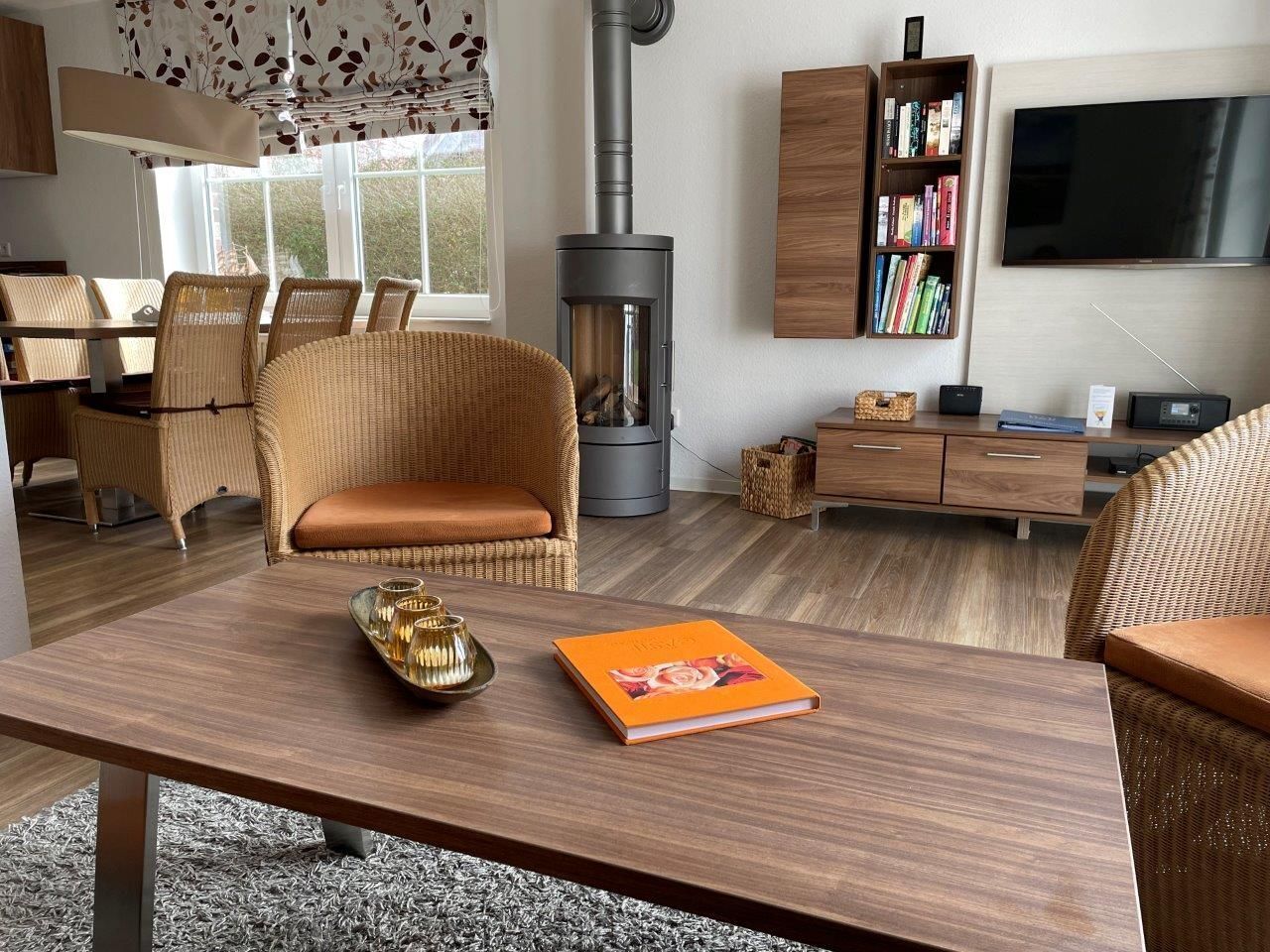 A modern living room with a large fireplace, wicker furniture, a wooden coffee table, and a bookshelf.