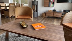 A modern living room with a large fireplace, wicker furniture, a wooden coffee table, and a bookshelf. - ROB 16 for 7 persons, approx. 86 sqm - Feriendorf Robbenplatte Burhave (3) (Butjadingen)