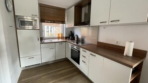 A modern kitchen with white cabinets, a microwave, stove, and a window with blinds. - ROB 16 for 7 persons, approx. 86 sqm - Feriendorf Robbenplatte Burhave (3) (Butjadingen)