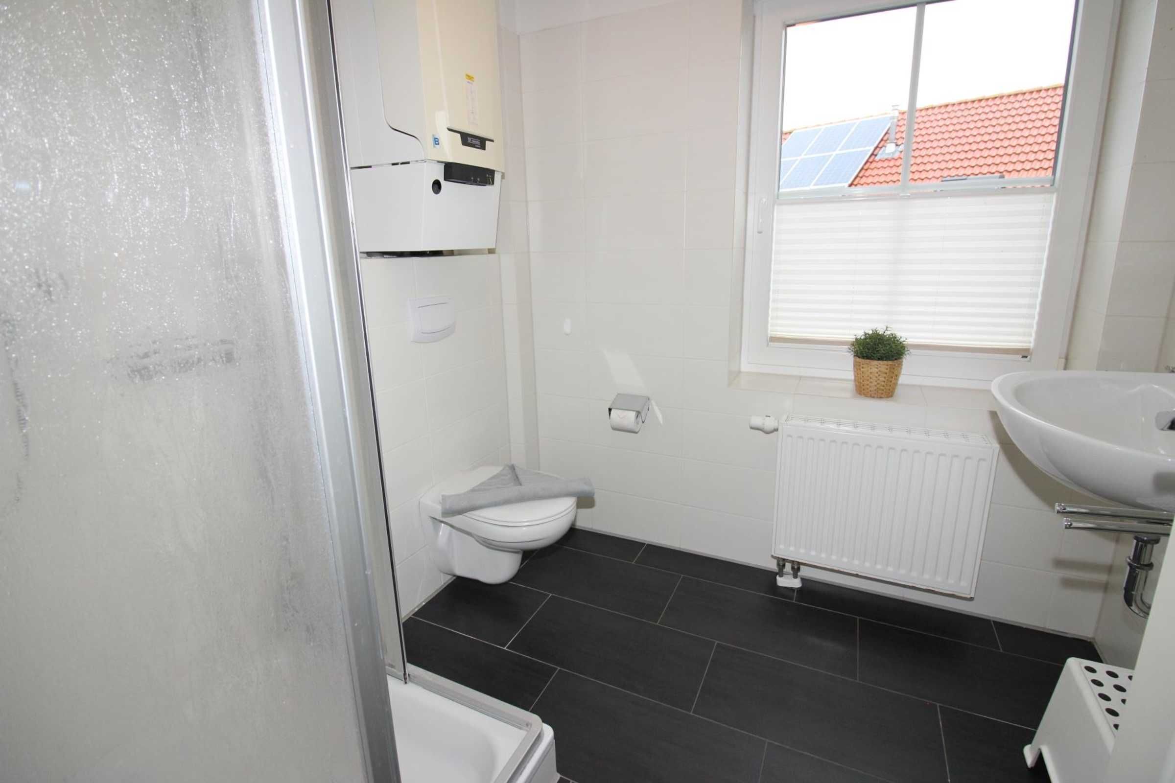 Ein Badezimmer mit Toilette, Waschbecken, Heizkörper und Fenster mit Blick auf ein Gebäude mit rotem Dach.
